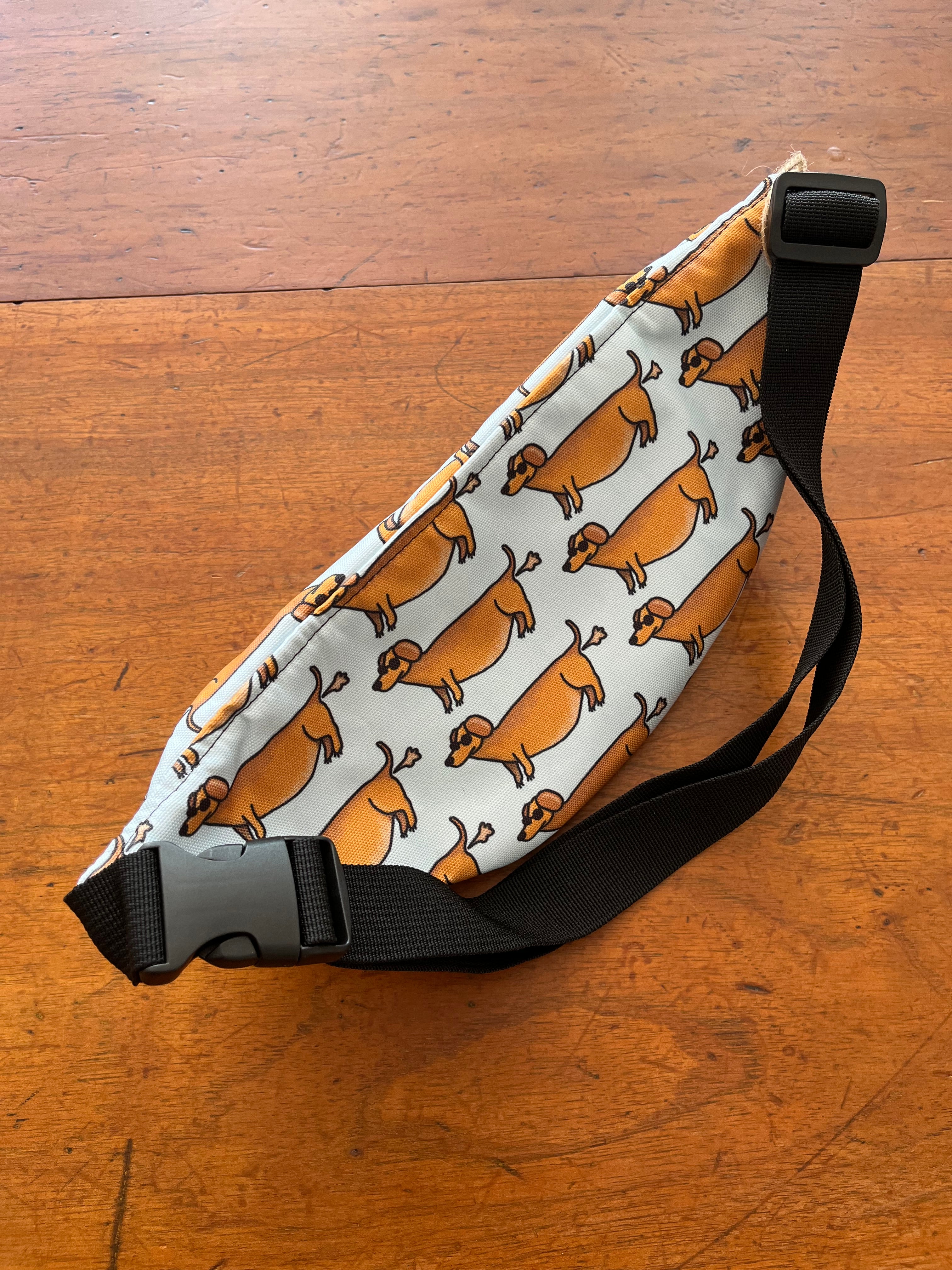 fanny pack met tekening van teckels die scheetjes laten door Anne Neuteboom cabaretier Anne Neut Boetiek