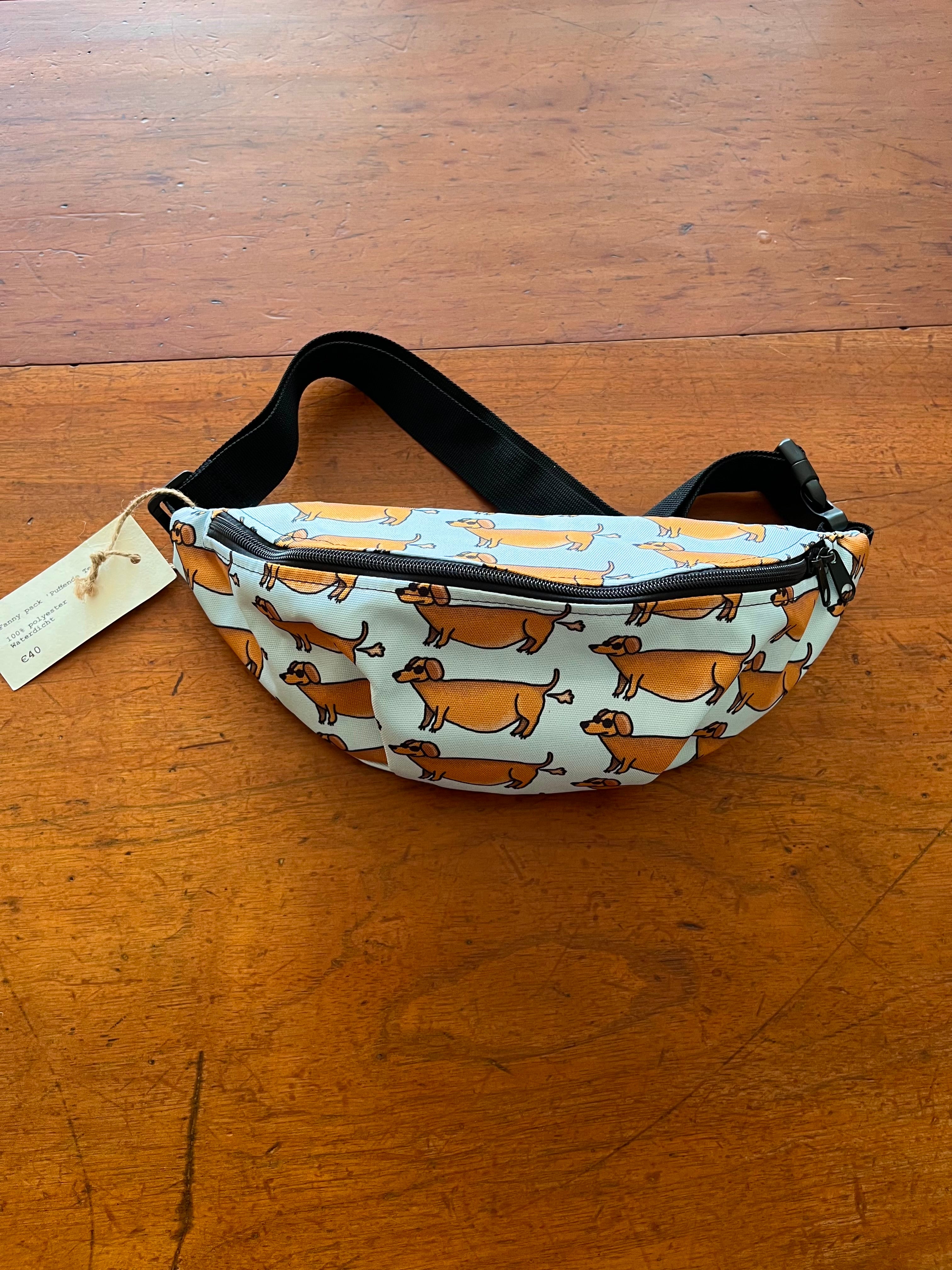 fanny pack met tekening van teckels die scheetjes laten door Anne Neuteboom cabaretier Anne Neut Boetiek